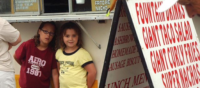 Ninie-year-old Samantha Angell and her sister Sydney Angell, 7, try to stay dry by squeezing under the counter of a vending stand as a light rain fell in downtown Tonganoxie. Heavy rains that started about 9 a.m. Saturday drastically reduced attendance at the annual event and made many vendors head home before the sun made an appearance in mid-afternoon. For more Tonganoxie Days pictures, see the photo gallery at right.