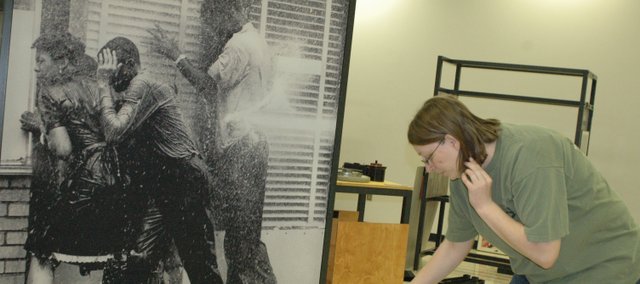 While assembling the exhibit, Michelle Wolfe sorts through exhibit information Monday near an image of civil rights protesters being blasted with a water hose. The “For All the World to See” exhibit at the Wyandotte County Historical Museum includes some graphic images from the era of the civil rights movement as well as images of blacks from popular culture. It opens to the public Monday.