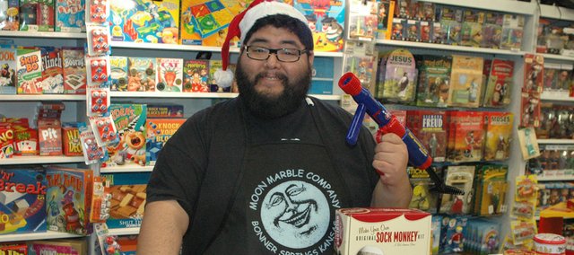 Jay Reyes, employee at Moon Marble Co., displays some of the best sellers at the store, including (from left on the table) the Marshmallow Blaster, which Reyes also is holding; the Sock Monkey; the Dashboard Zombie; and the Mug Shots shot glasses. With a wide array of games and toys for both adults and children, not to mention blown glass items and marbles, Reyes helps a lot of customers finds gifts. “Whether you’ve been naughty or nice, we’ve got you covered,” Reyes said.