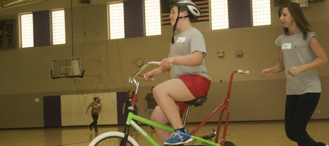 ICan Shine Bike Camp volunteer Paige Brant of Eudora races to keep up with Kaden Studley as he learns Thursday to weave through cones in a specially equipped training bicycle inside the Baldwin High School gymnasium.
