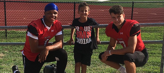 Shawnee Mission North football players Billy Conaway, left, and Noah Laird, right, take a photo with 8-year-old Bo Macan at the Indians' scrimmage on Friday. Conaway and Laird have organized a "Yards for Super Bo" fundraiser to support Macan, who battles rheumatoid arthritis, Type I diabetes, epilepsy and growth hormone deficiency as part of his rare condition.