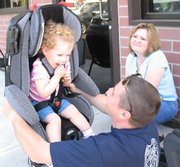 Officer Brian Duncan, a child passenger safety technician for the Lansing Police Department, lifts Anna Marlow, 20 months, while showing her mother, Jamie, how to test for a snug fit. Local police, fire and EMS services conducted free checks in an event put on by Leavenworth Online.