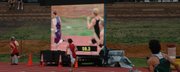 Bret Koch runs in front of a video board set up on the south side of the Cessna Stadium track during the boys 4x400 relay.