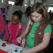 Maya Dodds (at left) and Sydney Gall, both in Basehor Girl Scout Troop 1274, learn the art of making castanets at the Panama booth put together by Basehor Girl Scout Troop 1545.