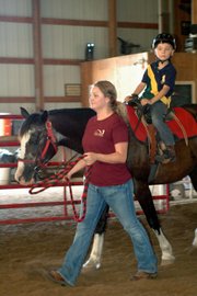 Charley Olsen looks ahead as a Due West staff member leads his horse around the indoor arena during his lesson Tuesday.